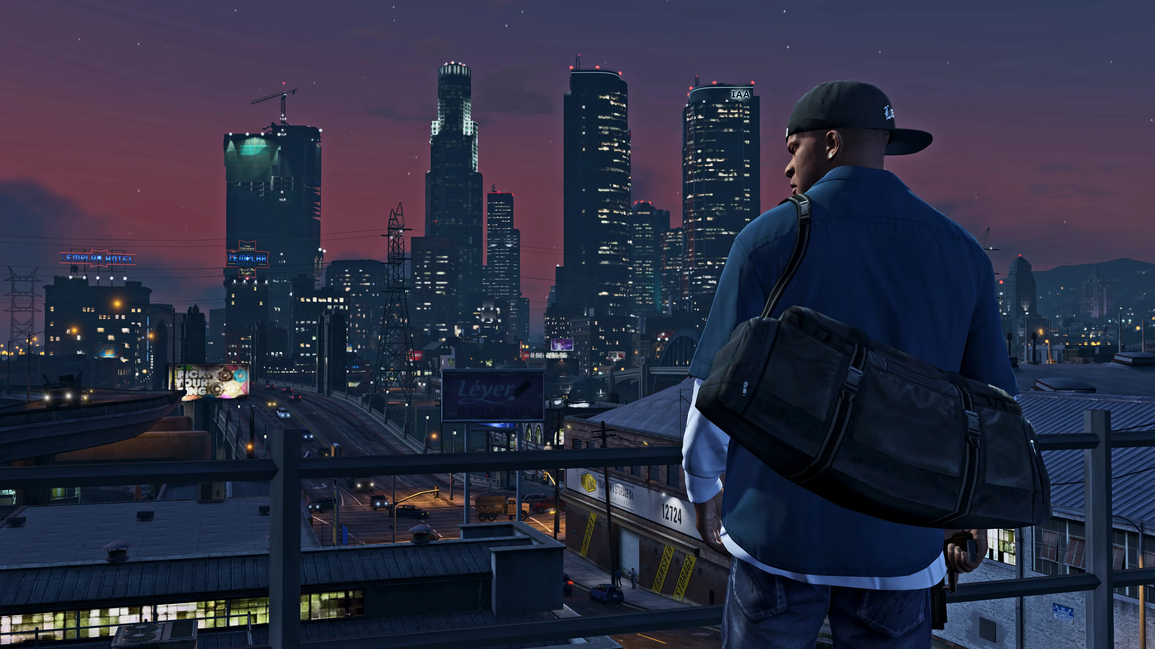 Franklin stands on a rooftop overlooking the illuminated Downtown Los Santos skyline at dusk.